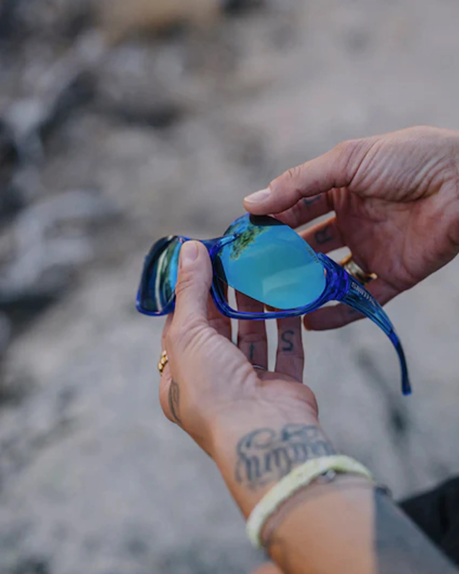 Blue-framed sunglasses with reflective blue lenses held in tattooed hands.