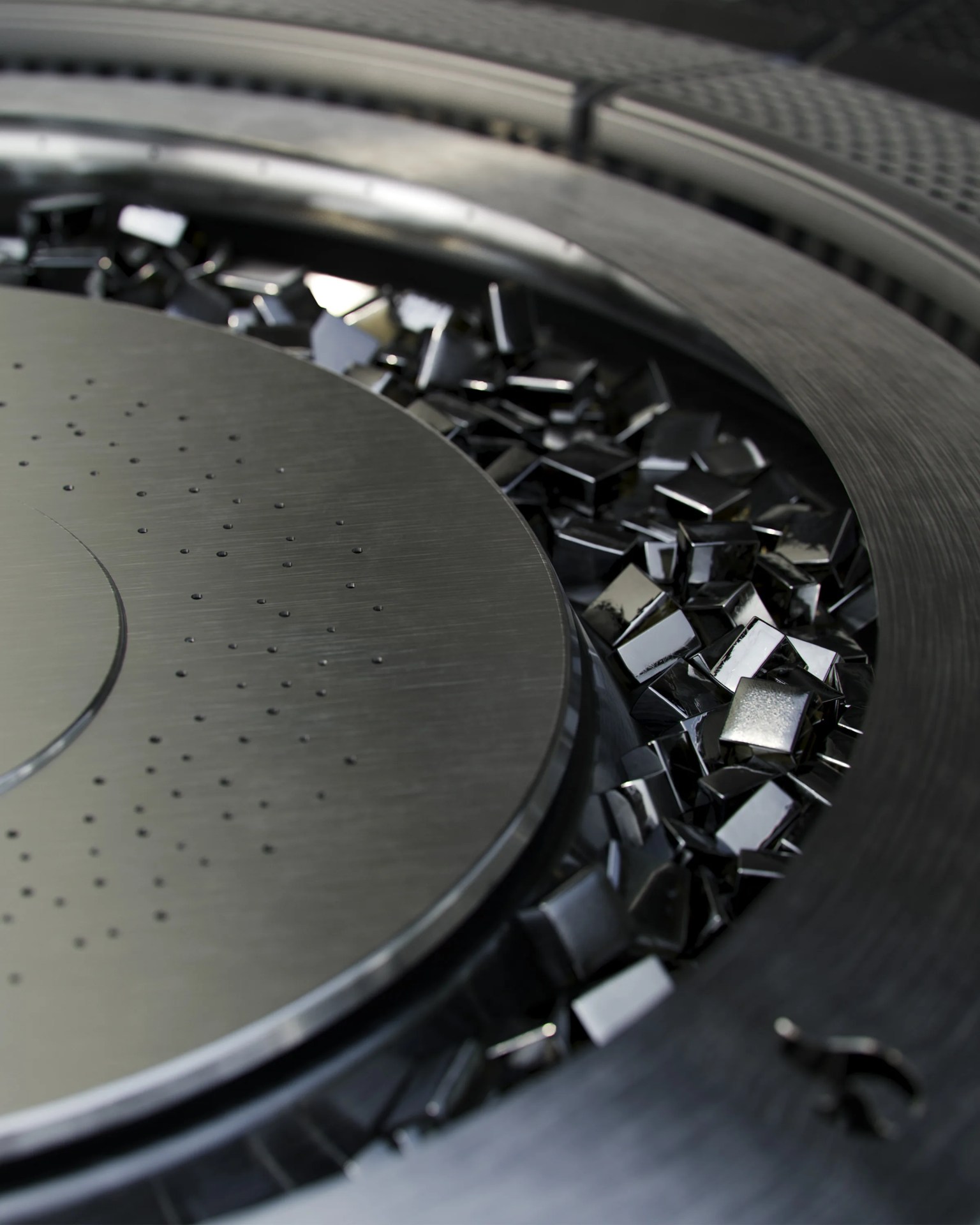 Close-up of a circular metallic object with small perforations surrounded by shiny, reflective black square pieces.