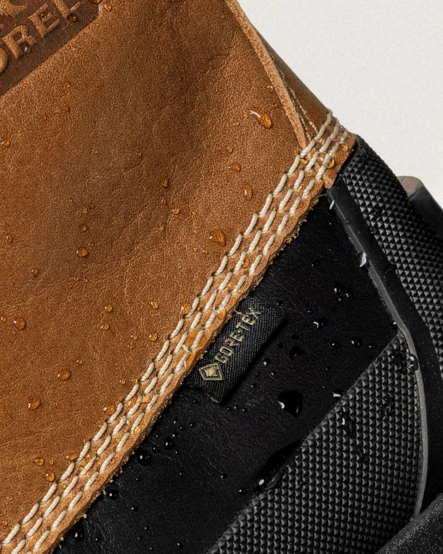 Close-up of a brown leather and black fabric shoe with Gore-Tex tag and water droplets on the surface.