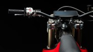 Close-up of a motorcycle handlebar with black grips, silver controls, and a mounted smartphone on a red and carbon fiber tank.