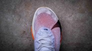 White and orange Nike running shoe with mesh upper on a concrete surface.