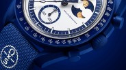 Close-up of a blue Moonswatch with a white dial, moon phase indicator, and textured blue fabric strap with the Omega x Swatch logo.