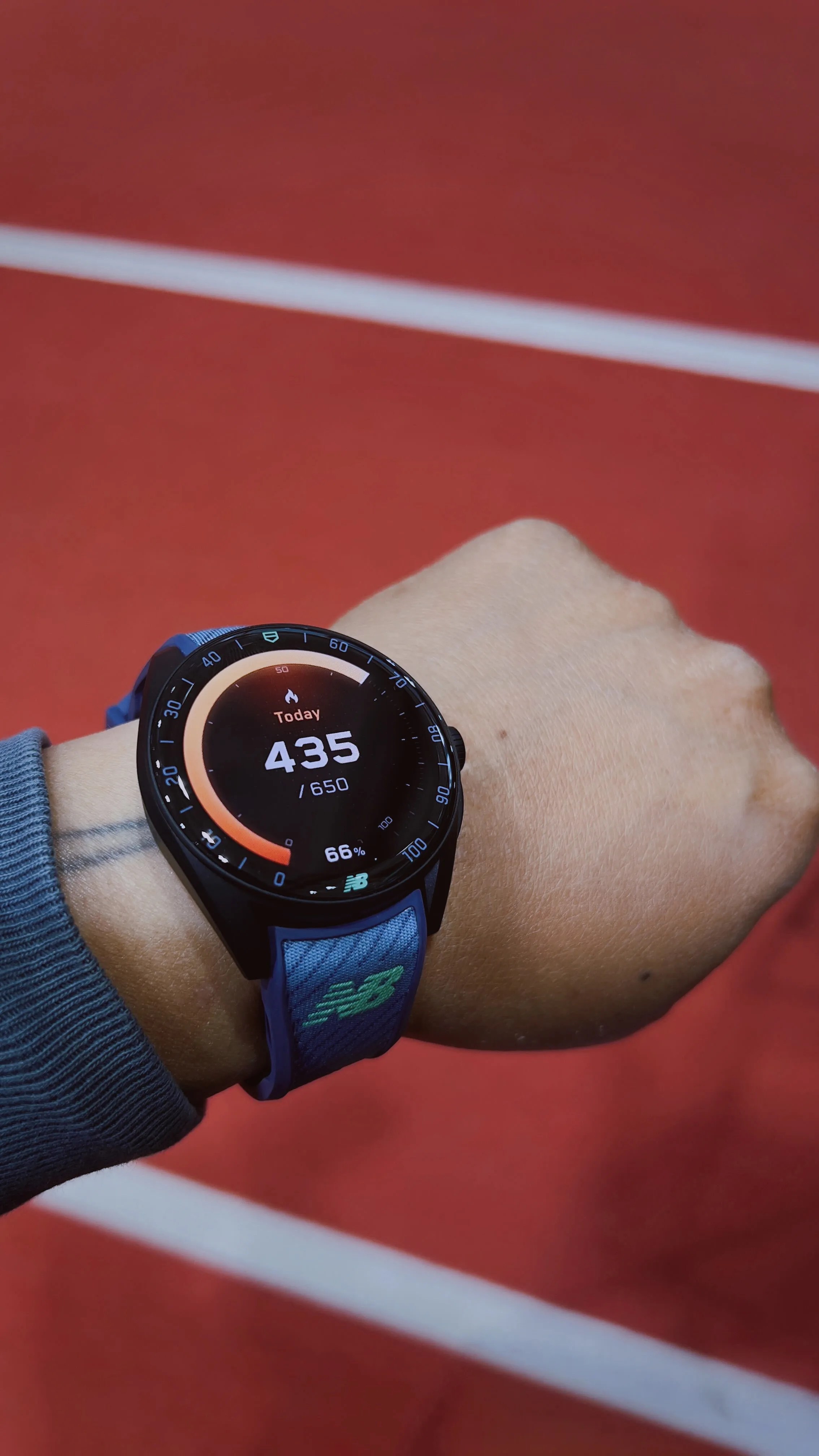Smartwatch with a blue New Balance fabric strap showing 435 of 650 calories burned on a wrist.