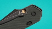 Black folding knife with textured handle and Tenable logo on the blade against a turquoise background.