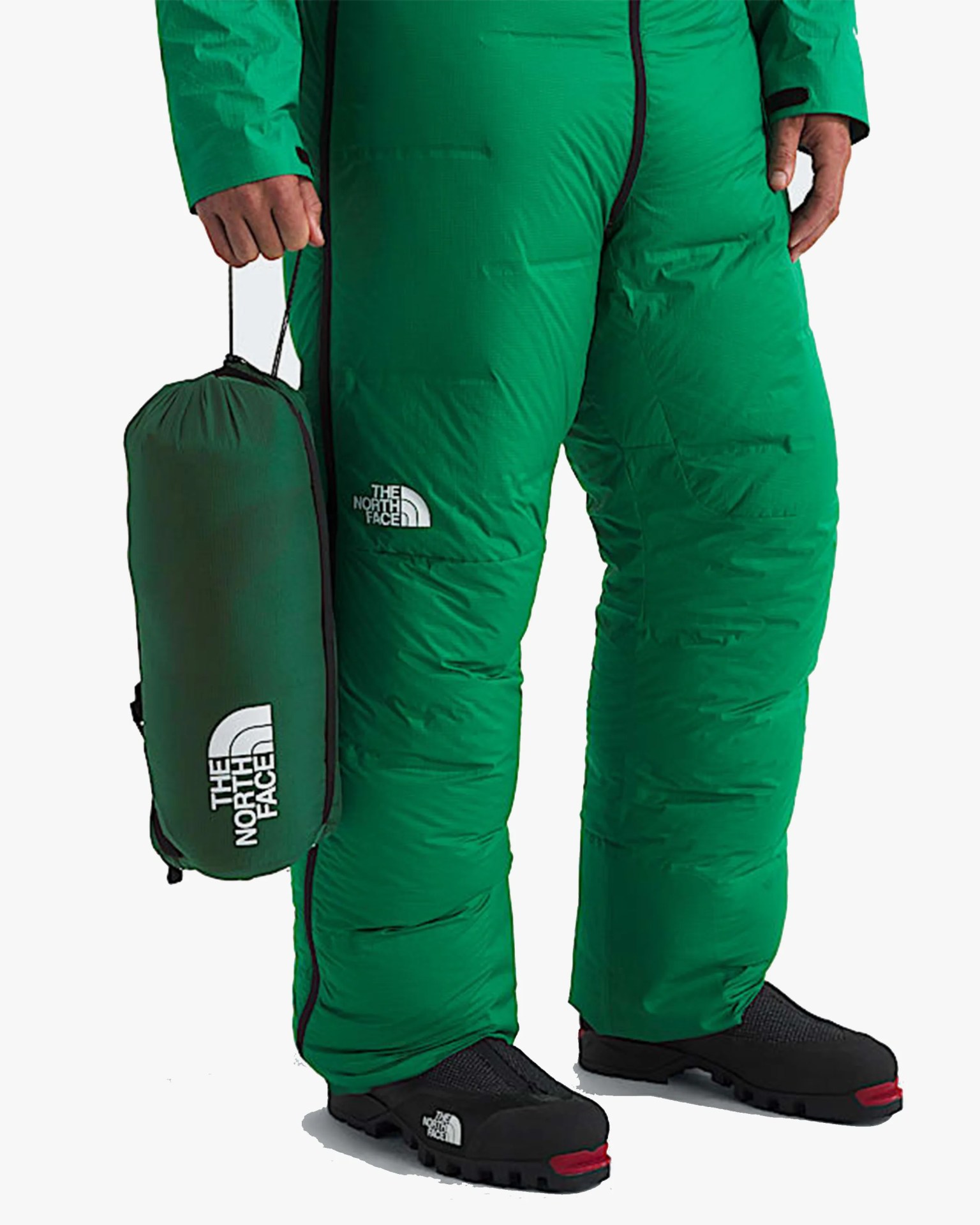 Green insulated pants with black zippers and The North Face logo worn with black and red shoes, holding a matching green stuff sack.
