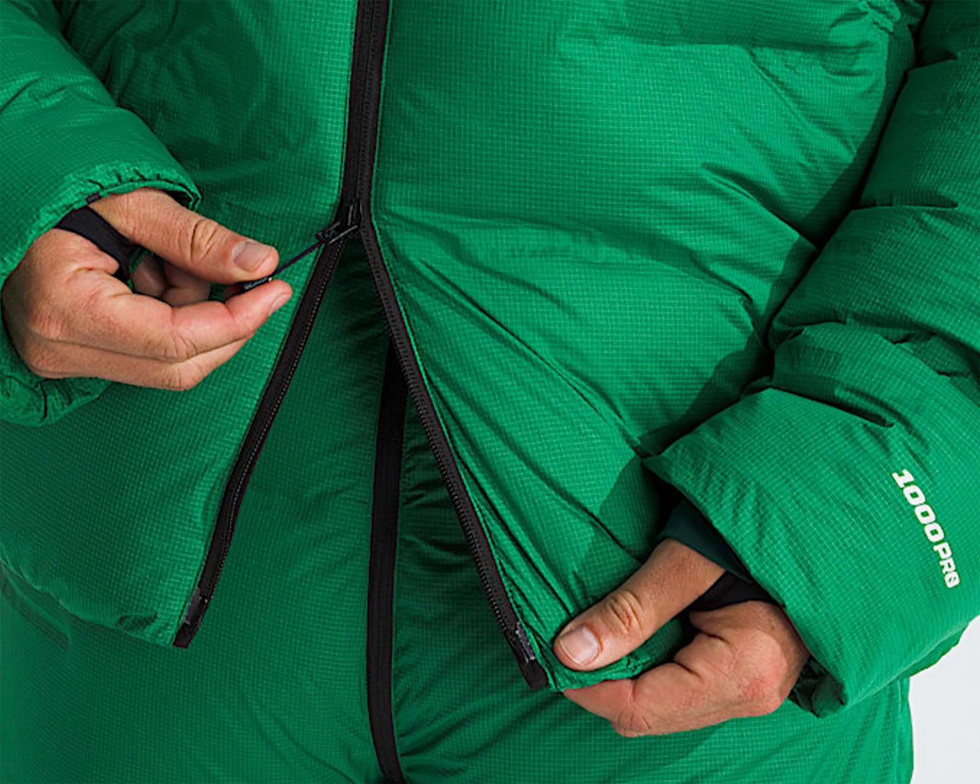 Close-up of hands zipping a green puffer jacket with "1000 PRO" printed on the sleeve.