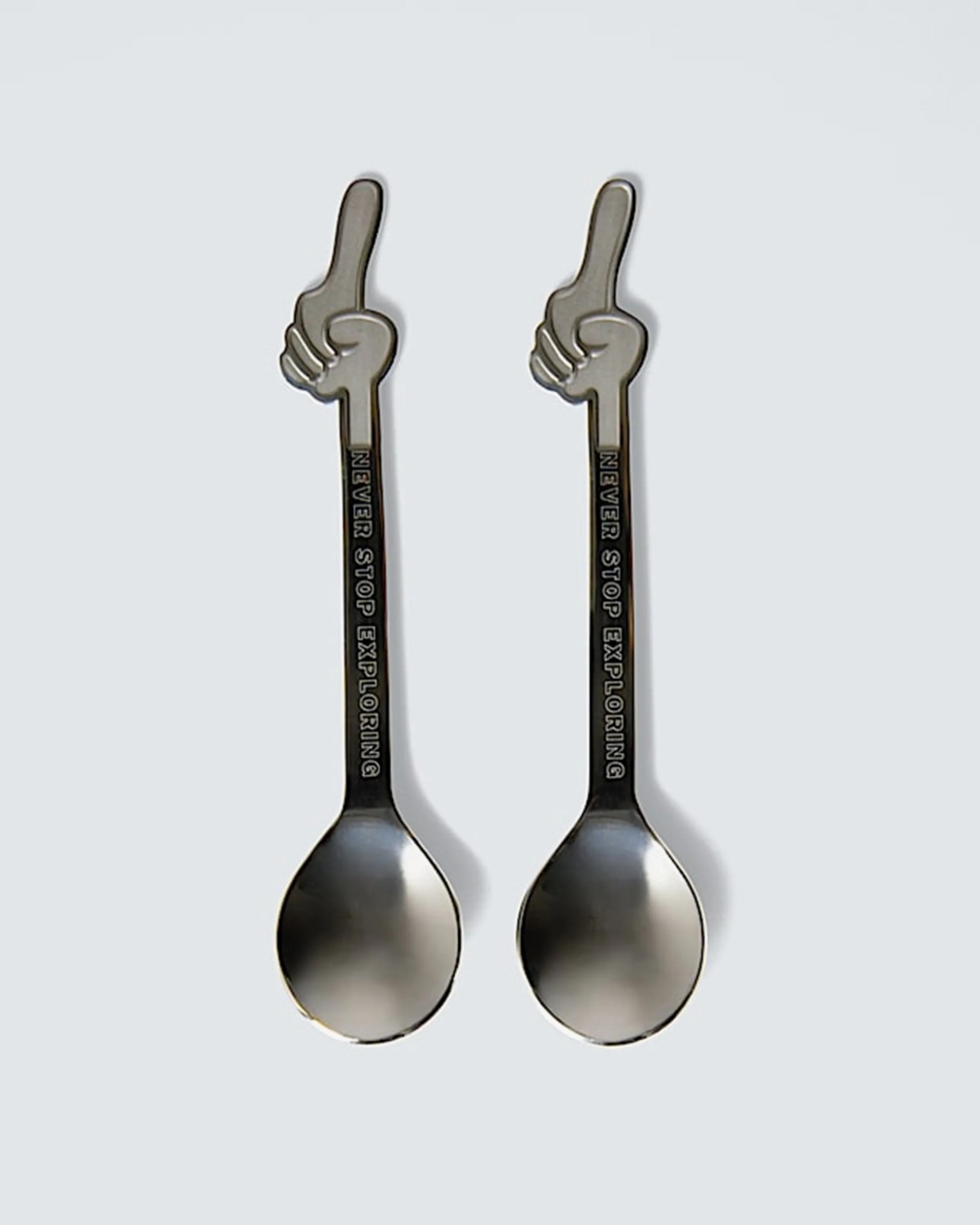 Two silver spoons with handles shaped like hands pointing upward and the text "NEVER STOP EXPLORING" on the handles.