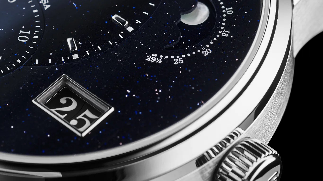 Close-up of a luxury watch with a dark blue speckled dial, silver markers, a date window showing "25," and a polished silver crown.
