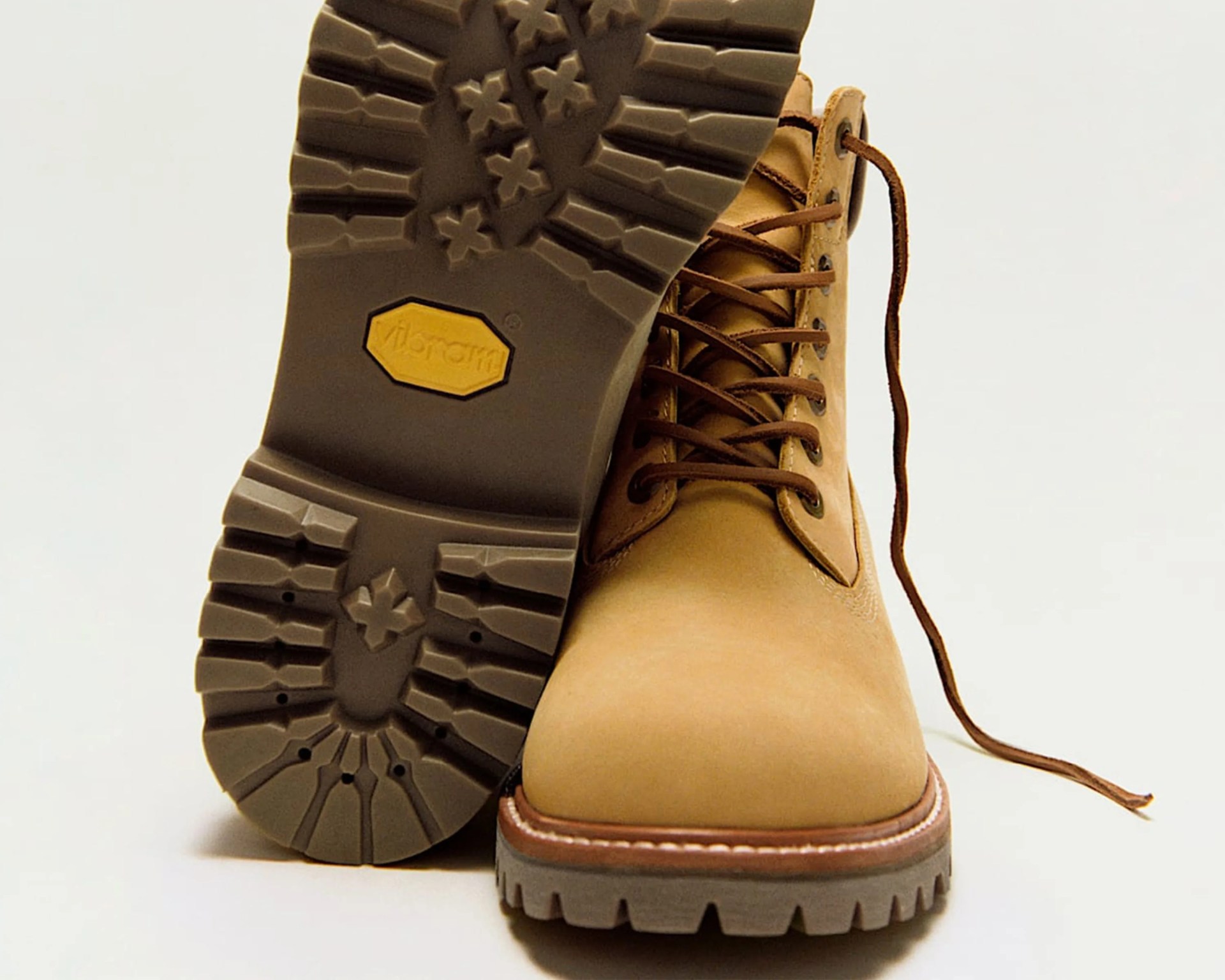 Tan leather lace-up boot with thick brown Vibram sole, one boot showing tread pattern.