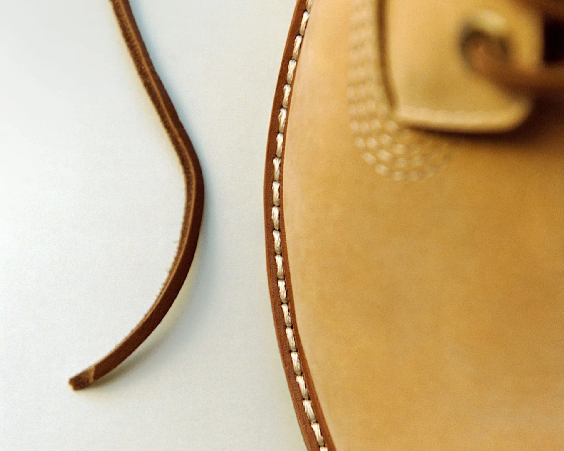 Close-up of tan leather shoe with white stitching and a brown leather lace on a light surface.
