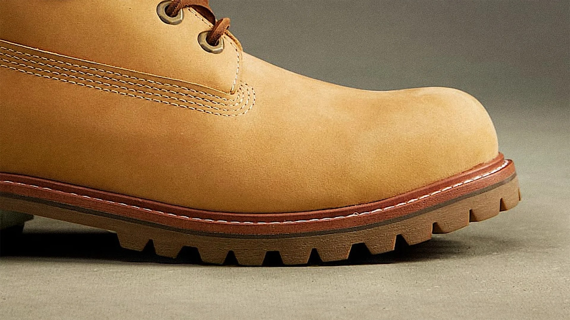 Tan leather work boot with thick brown lug sole and metal eyelets on a gray surface.