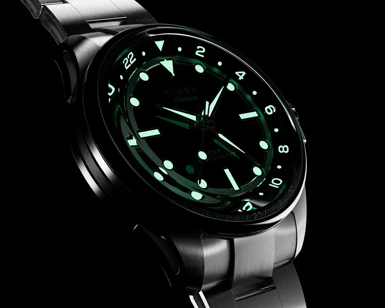 Stainless steel Timex wristwatch with glowing green luminescent markers and hands on a black dial.
