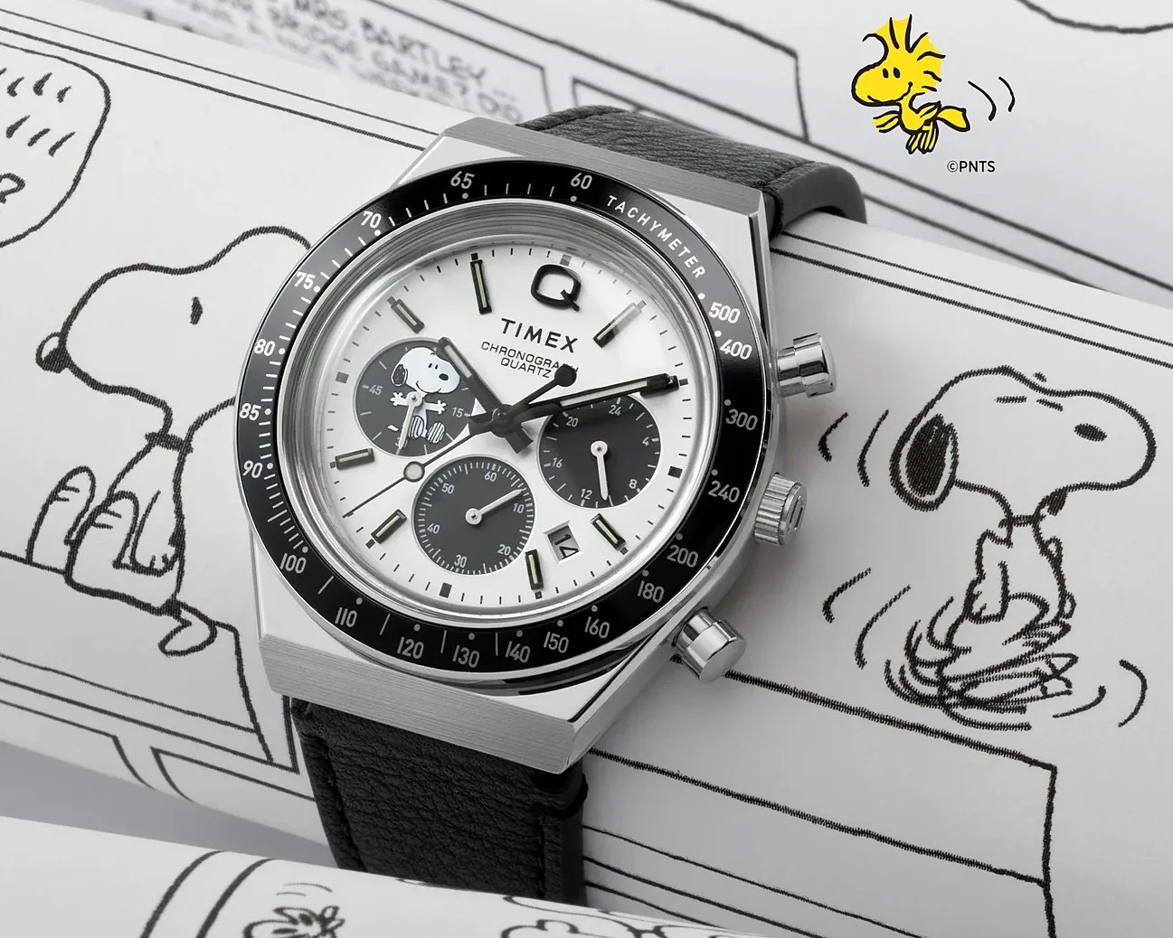 Silver Timex chronograph watch with black tachymeter bezel and Snoopy illustration on white dial, black leather strap.