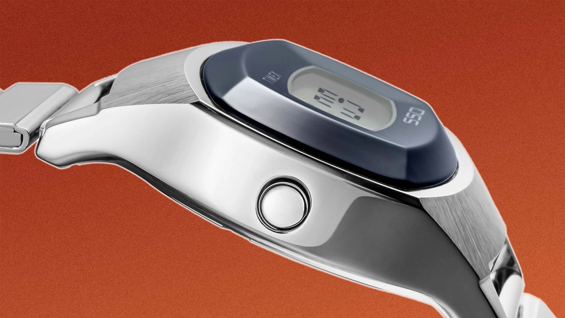 Close-up of a silver digital wristwatch with a blue bezel and a single round button on the side against a rust-colored background.
