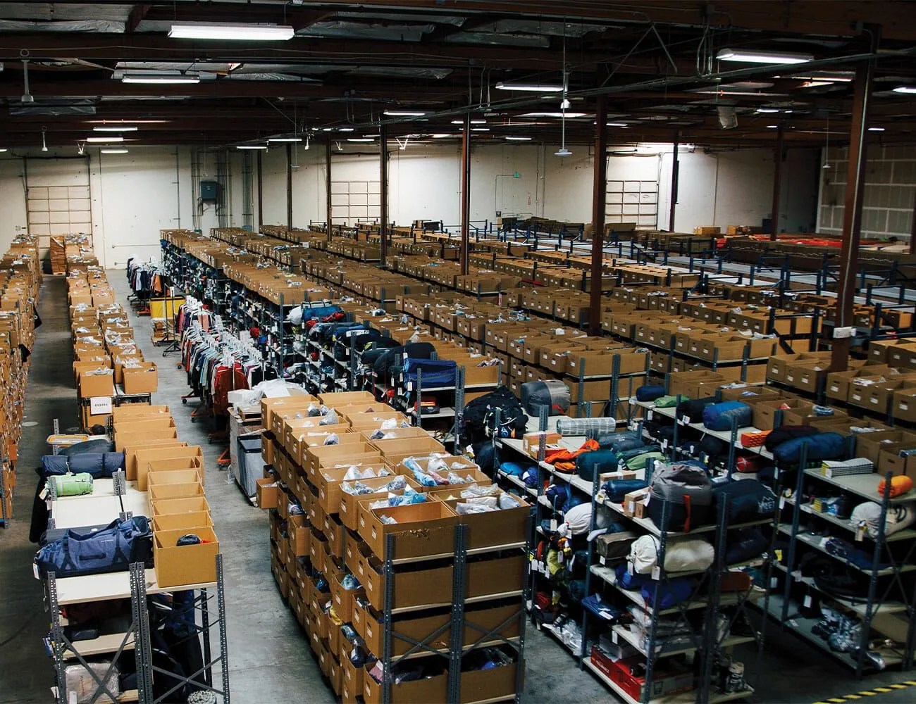 Large warehouse filled with metal shelves holding numerous brown cardboard boxes and some clothing items.