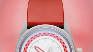 Silver watch with a white dial, red geometric hour and minute hands, and a red strap on a pink background.