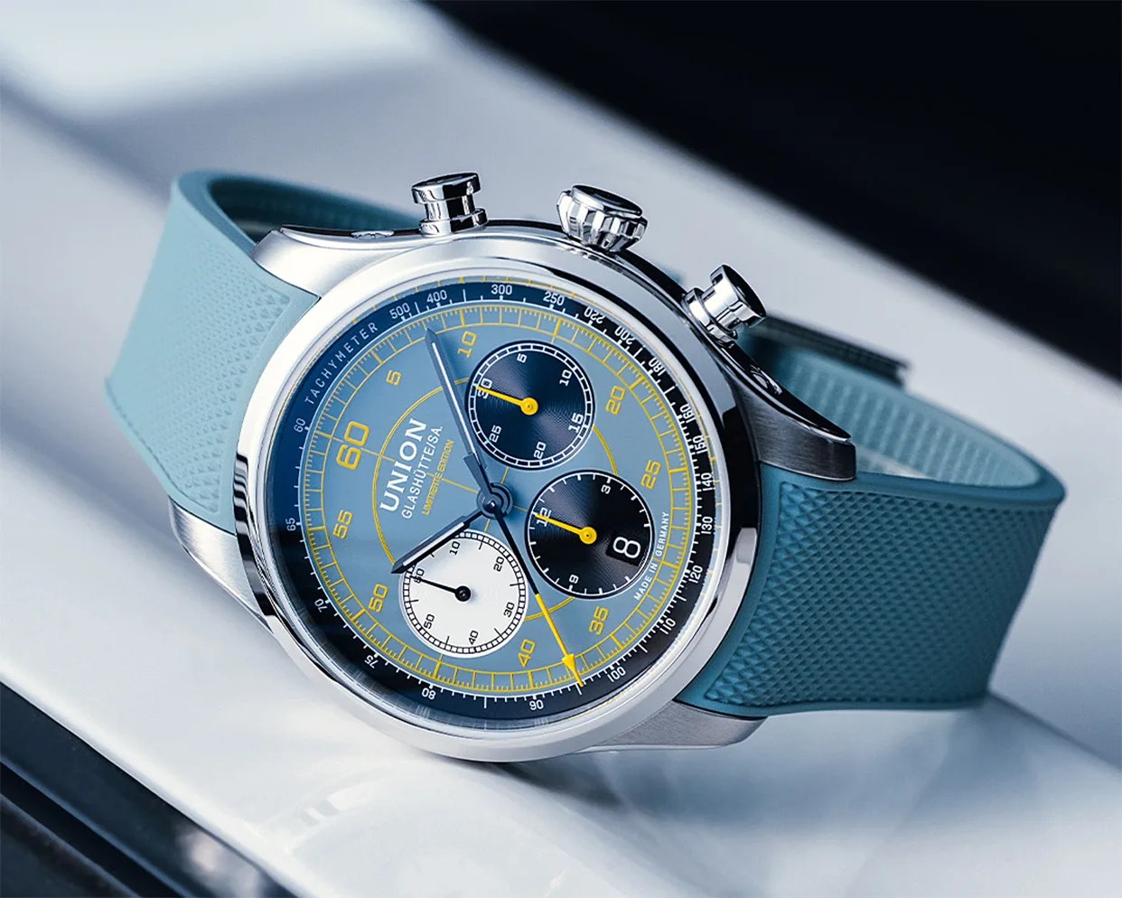 Union Glashütte chronograph watch with blue dial, yellow accents, and textured blue rubber strap.