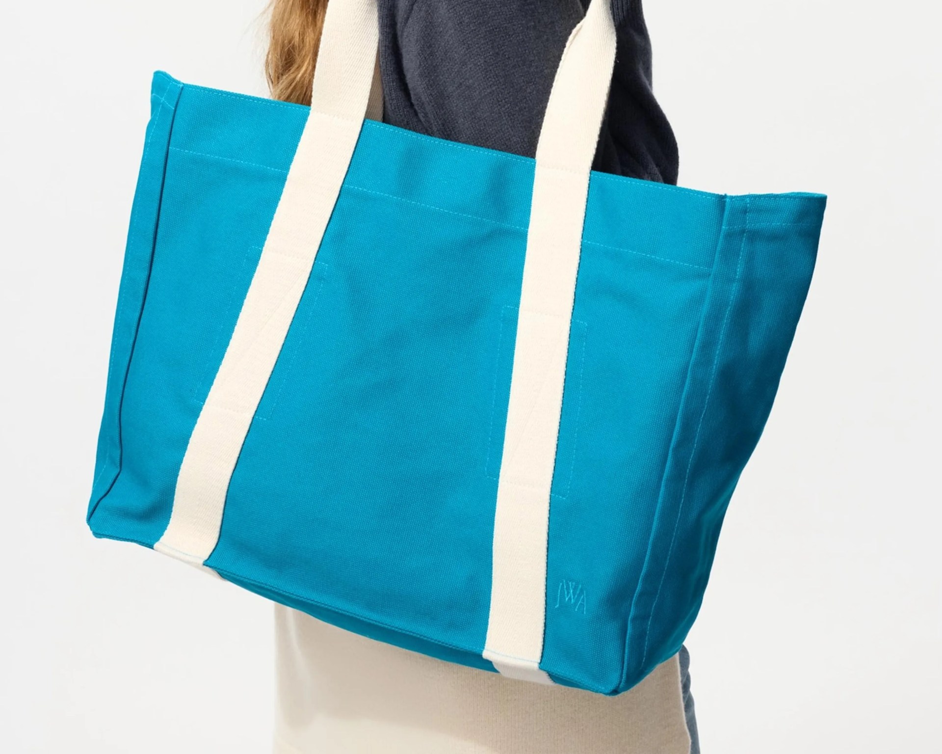 Bright blue canvas tote bag with wide off-white straps worn over a shoulder.