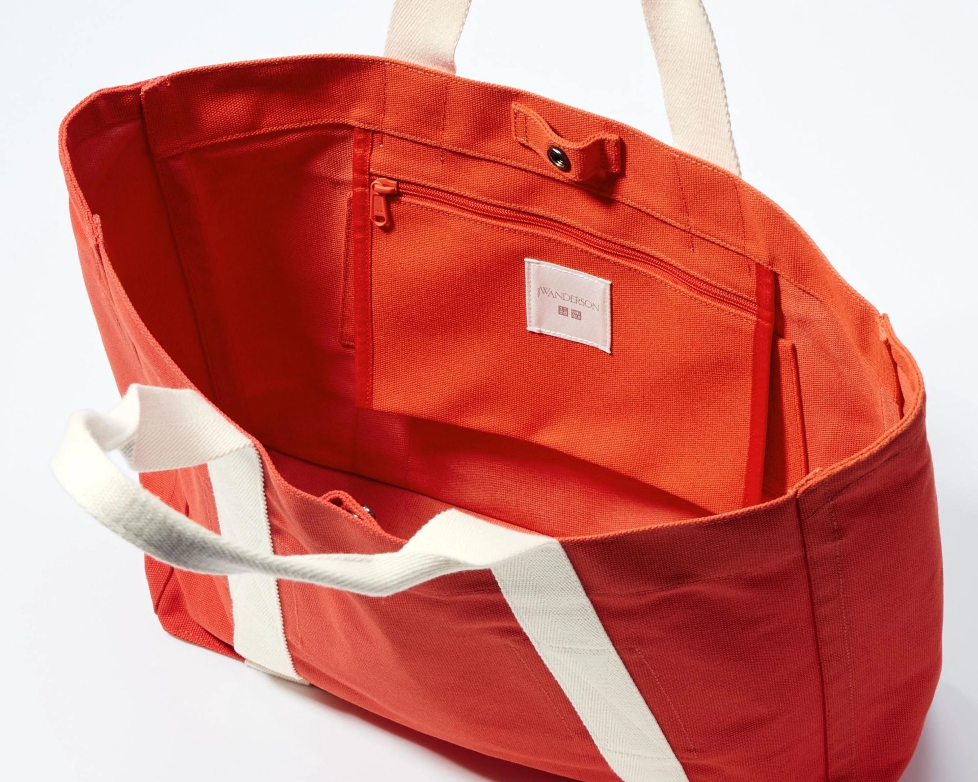 Open red canvas tote bag with white handles and interior zippered pocket labeled JW Anderson.