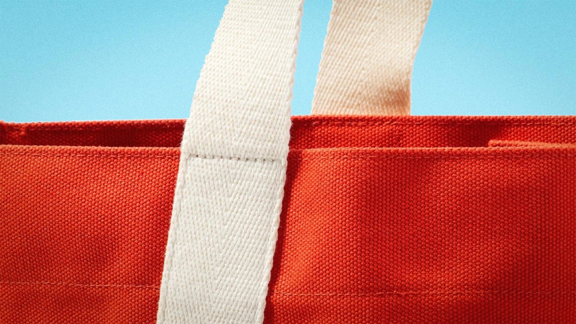 Close-up of an orange canvas tote bag with white fabric handles against a blue background.