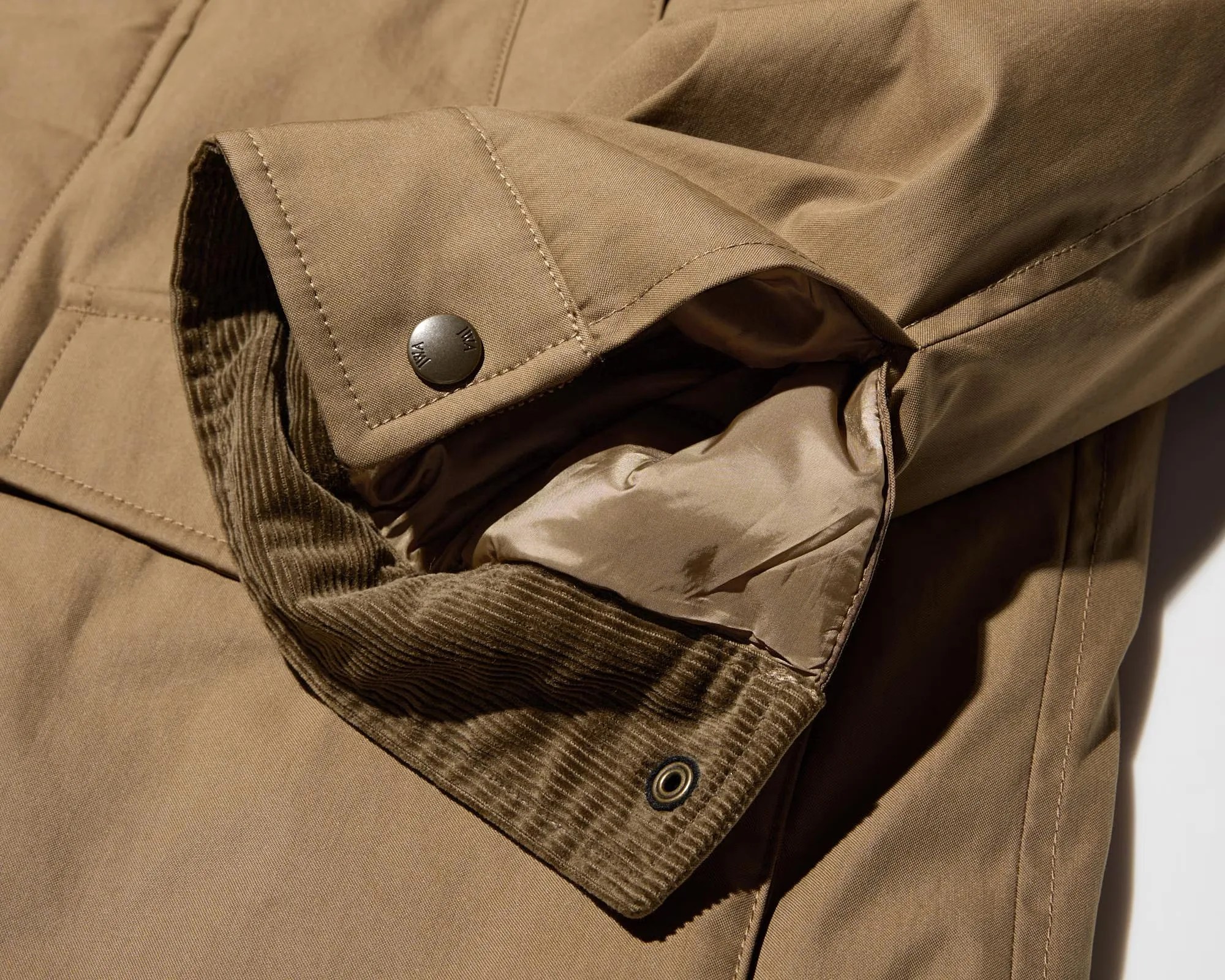 Close-up of a tan jacket sleeve with a snap button cuff and corduroy inner lining.
