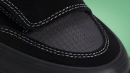 Close-up of black sneaker toe with textured fabric and white double stitching on black suede.