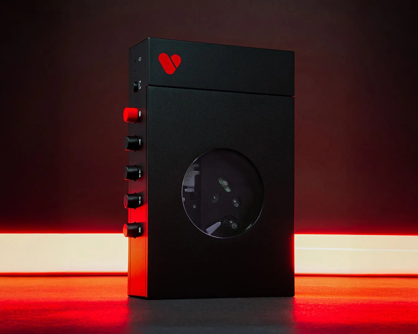 Black rectangular electronic device with a circular window and red and black knobs on the side, lit by red light.