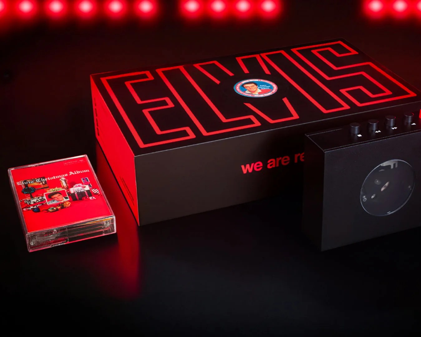 Black and red Elvis box set with cassette tape and black cassette player on a dark surface.