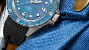 Close-up of a blue dial wristwatch with a black textured strap resting on blue fabric.