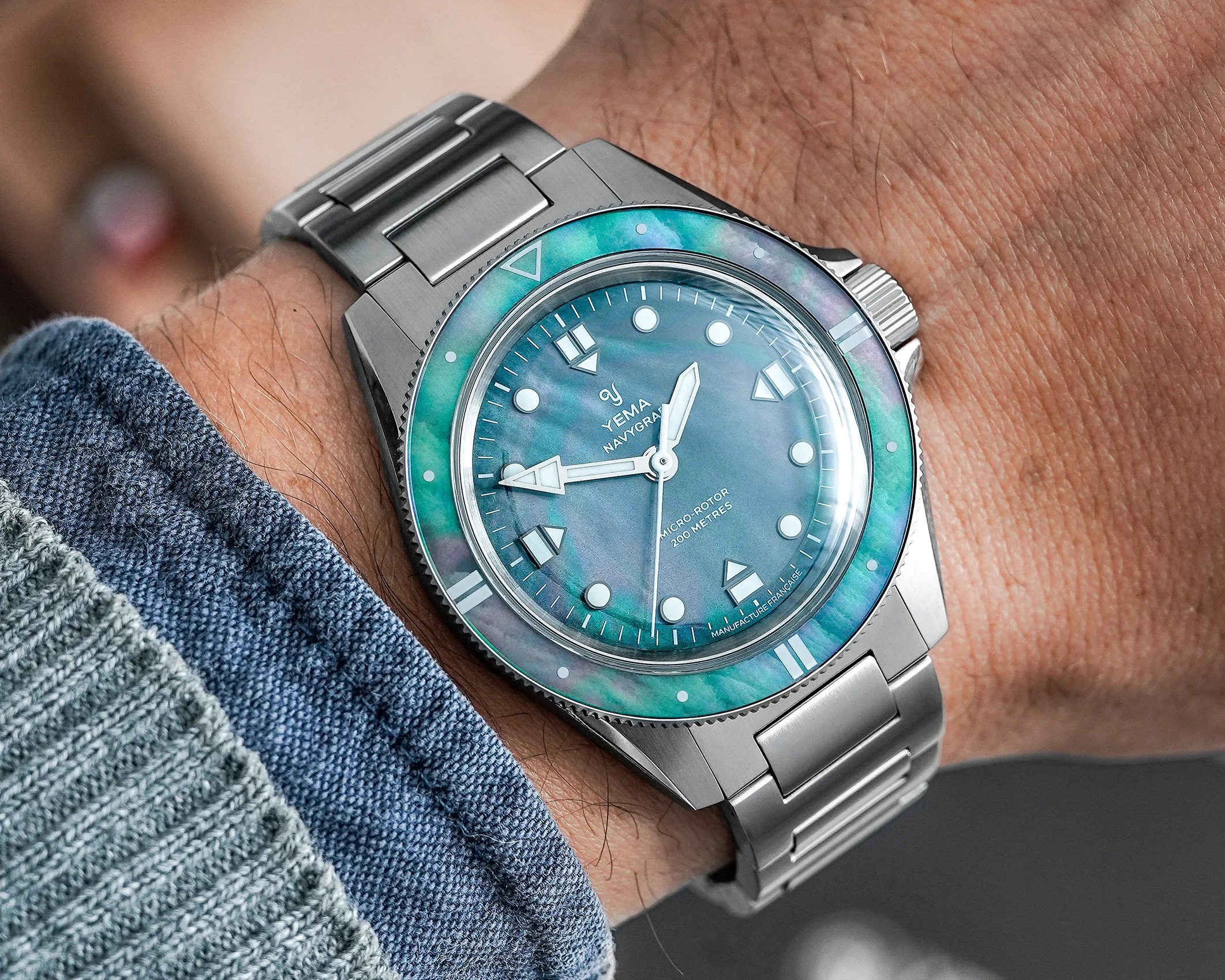 Stainless steel Yema Navygraf wristwatch with blue-green mother-of-pearl dial and bezel on a wrist.