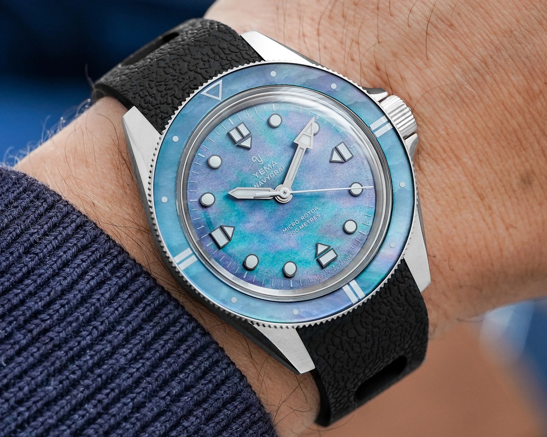 Silver Yema Navygraf wristwatch with iridescent blue dial and black textured strap worn on a wrist.