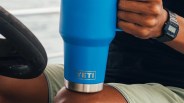 Blue YETI insulated tumbler held by a person wearing a black digital watch and light green shorts.