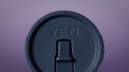 Dark blue YETI branded plastic lid with a sliding closure on a purple background.