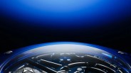 Close-up of a blue watch bezel with visible "EL PRIMERO 8612" engraving and metallic watch hands under a curved crystal.