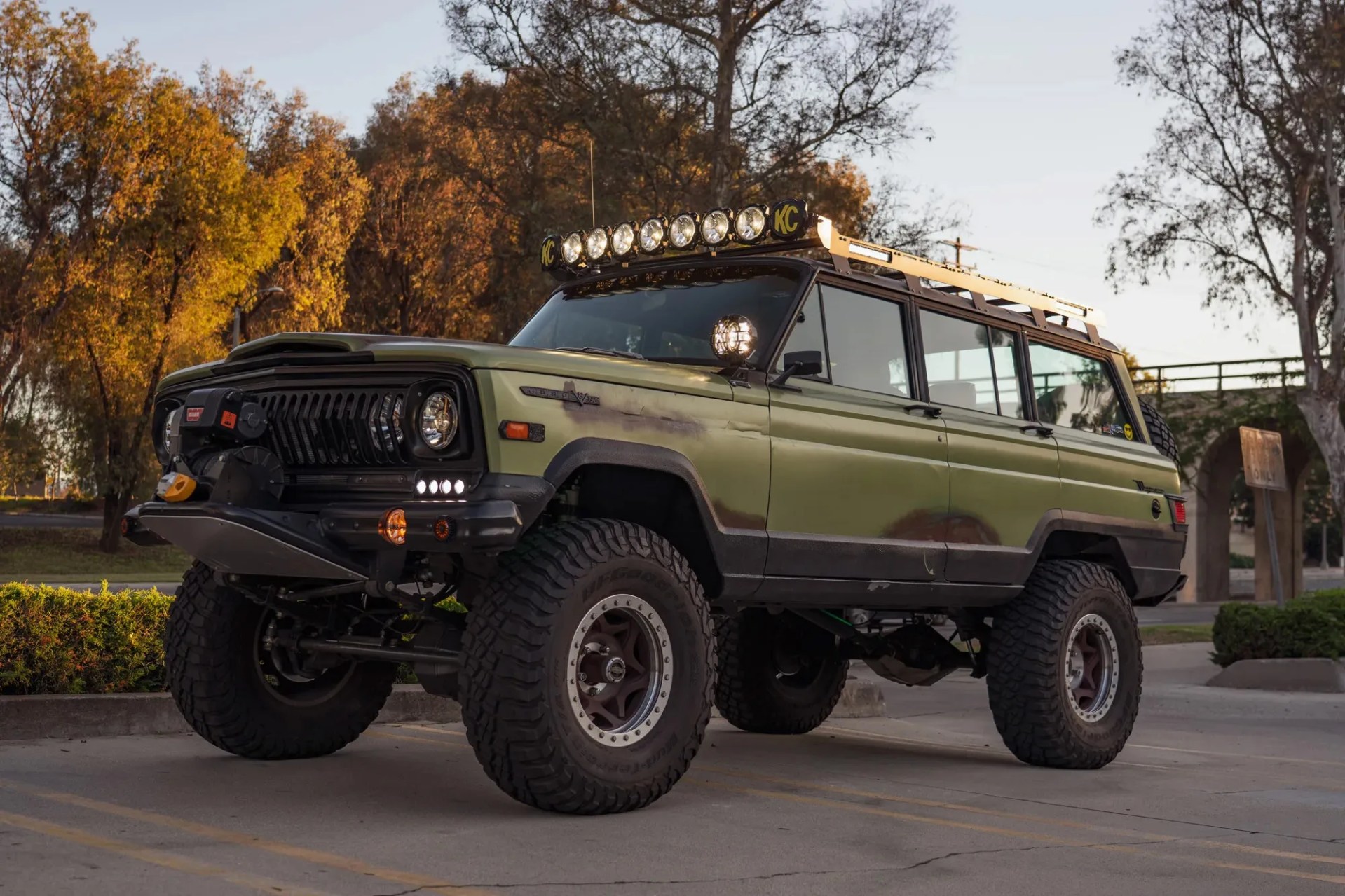 Green vintage off-road SUV with large tires, roof rack, and multiple front auxiliary lights parked outdoors.