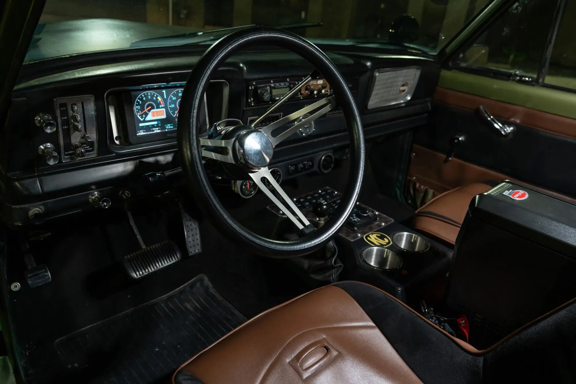 Interior of a vintage car with a black steering wheel, digital dashboard, brown leather seats, and center console with cup holders.
