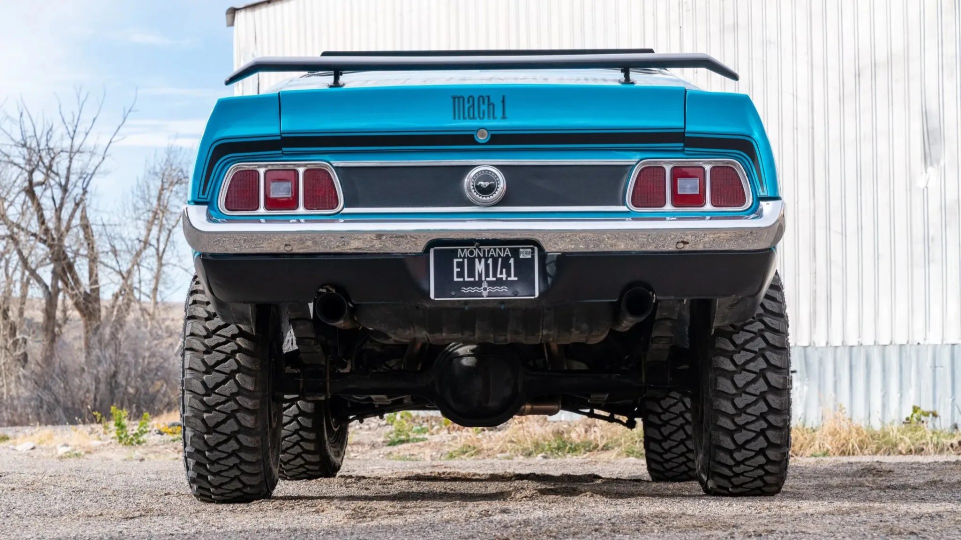 Rear view of a blue Ford Mustang Mach 1 with large off-road tires and Montana license plate ELM141.