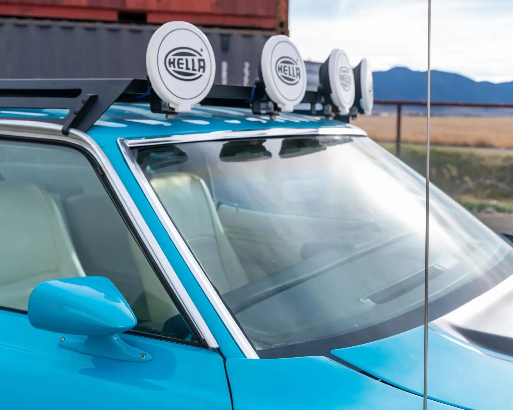 Blue car with white interior and four round Hella off-road lights mounted on the roof rack.