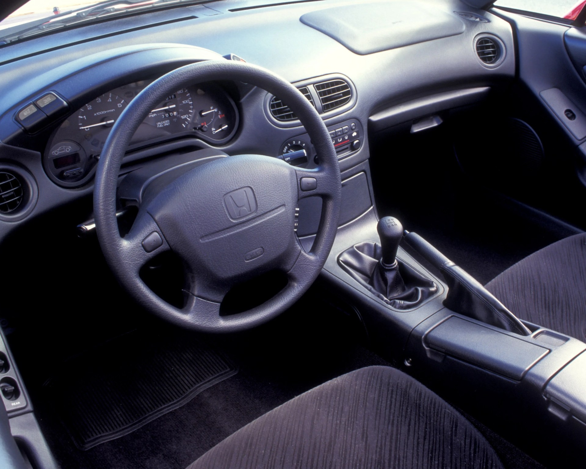 Black Honda car interior with a leather-wrapped steering wheel, manual gear shift, and fabric seats.
