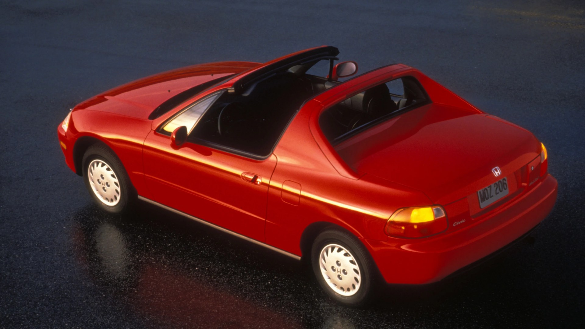 Red Honda Civic del Sol convertible with the roof partially retracted on wet pavement.