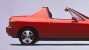 Red two-door convertible car with silver alloy wheels and black interior, shown from the side.