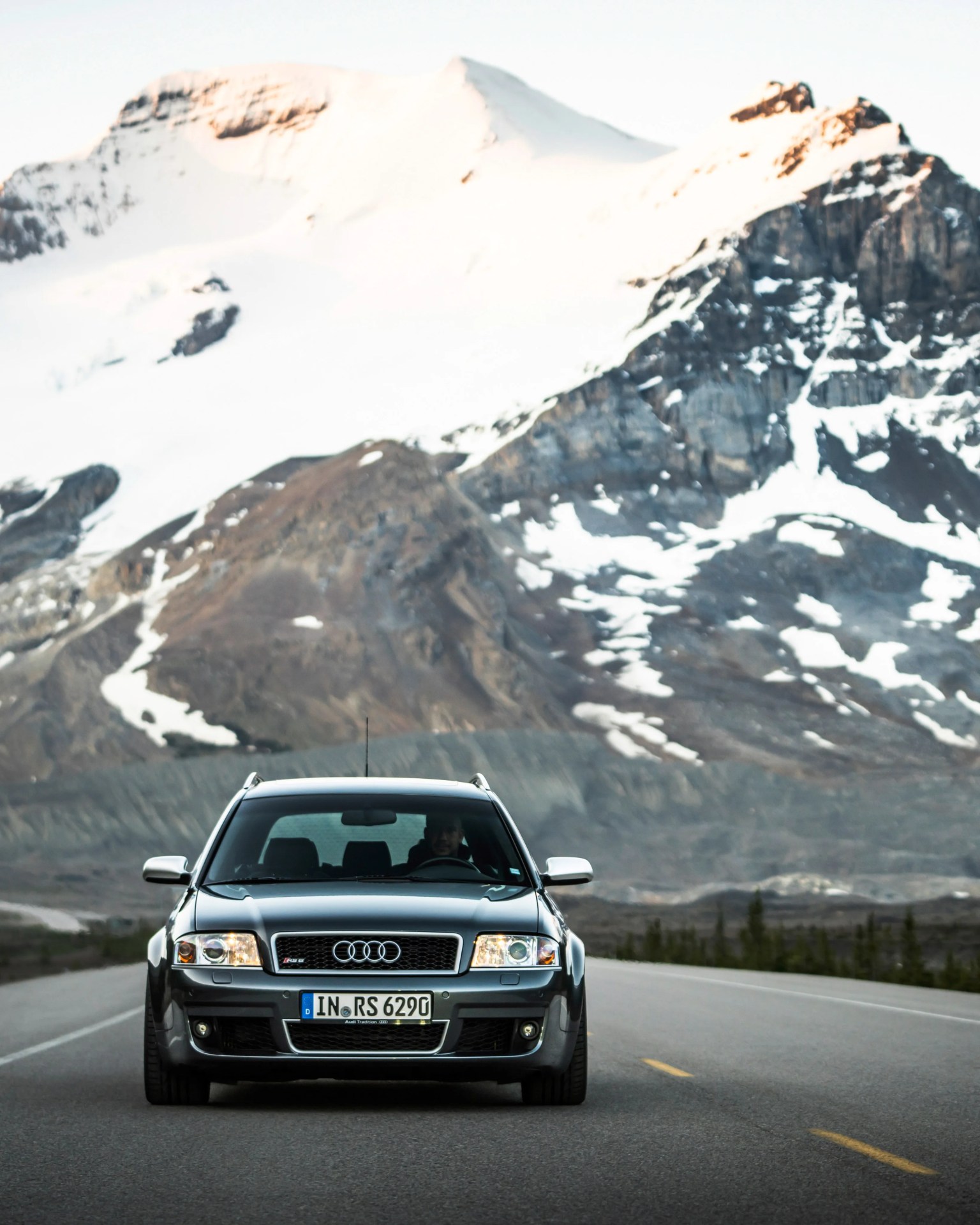 Black Audi RS4 sedan on an empty road with snow-capped mountains in the background.