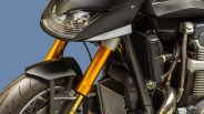 Close-up of a motorcycle front suspension with gold forks, black fender, headlight, and engine components.