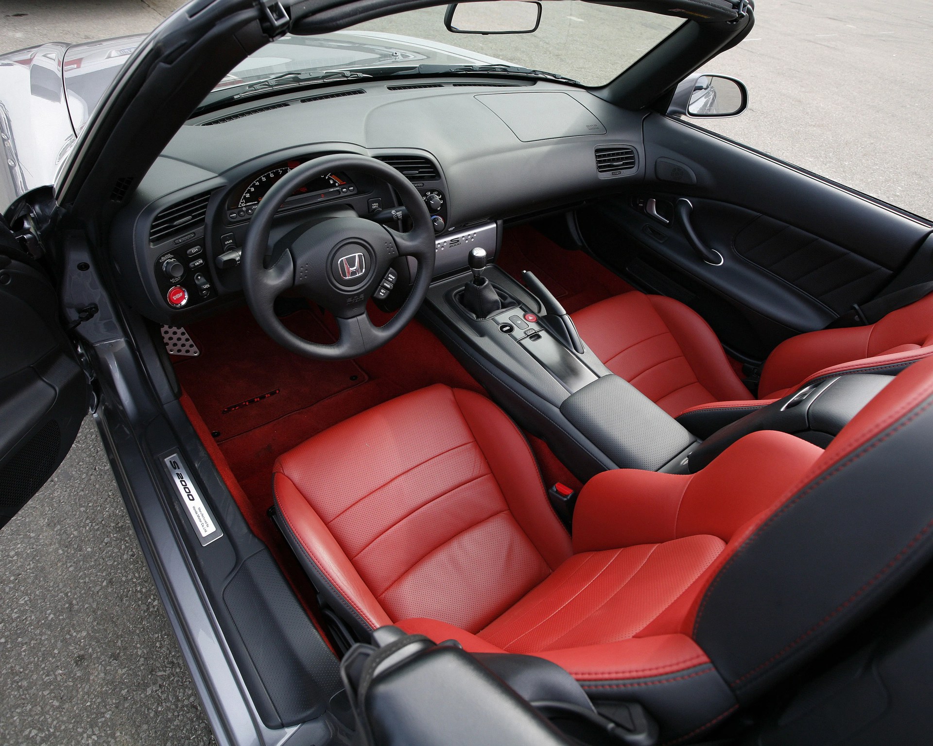 Convertible car interior with red leather bucket seats, black dashboard, and manual gear shift.