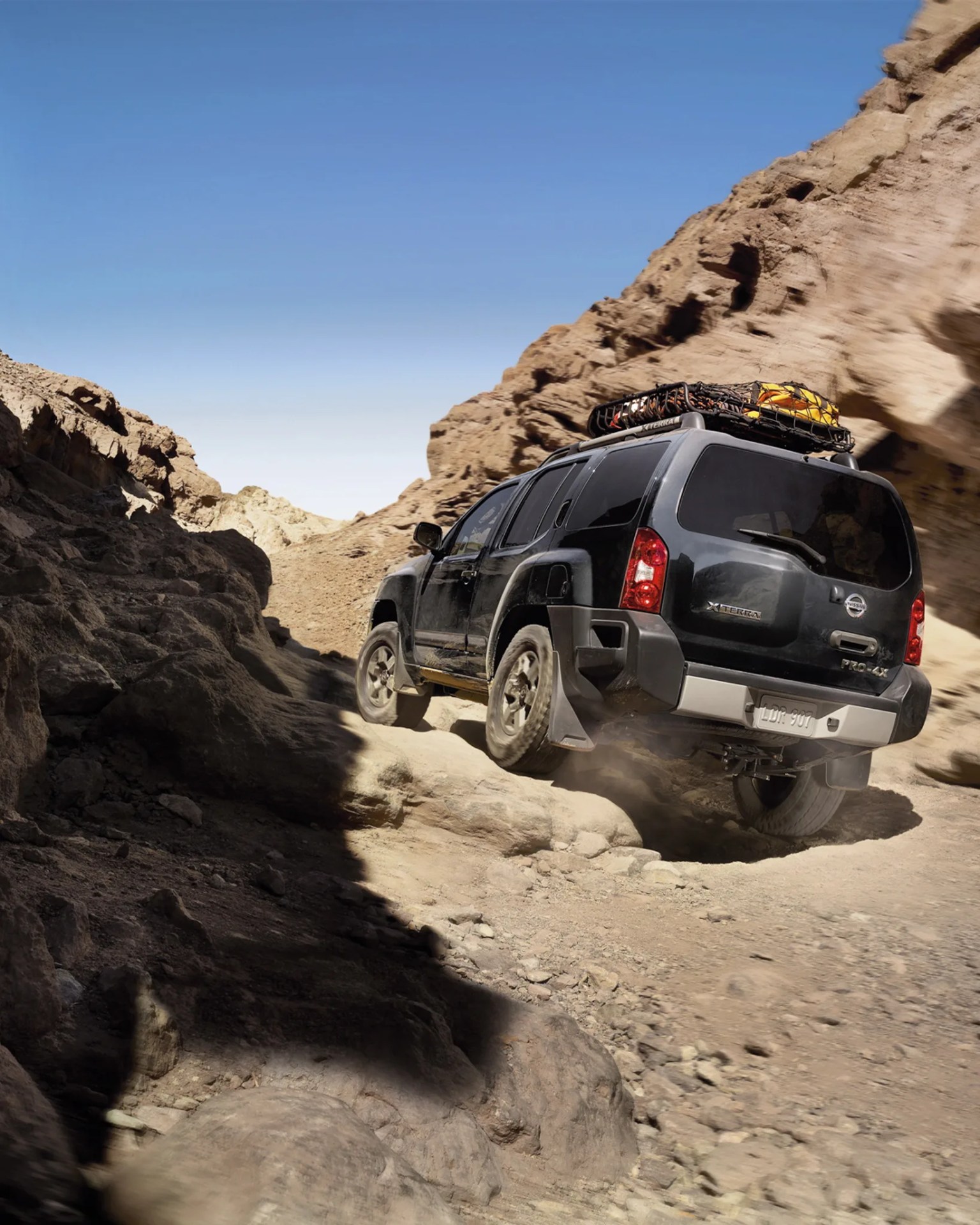Black Nissan Xterra Pro-4X SUV with roof rack carrying gear driving on rocky desert terrain.