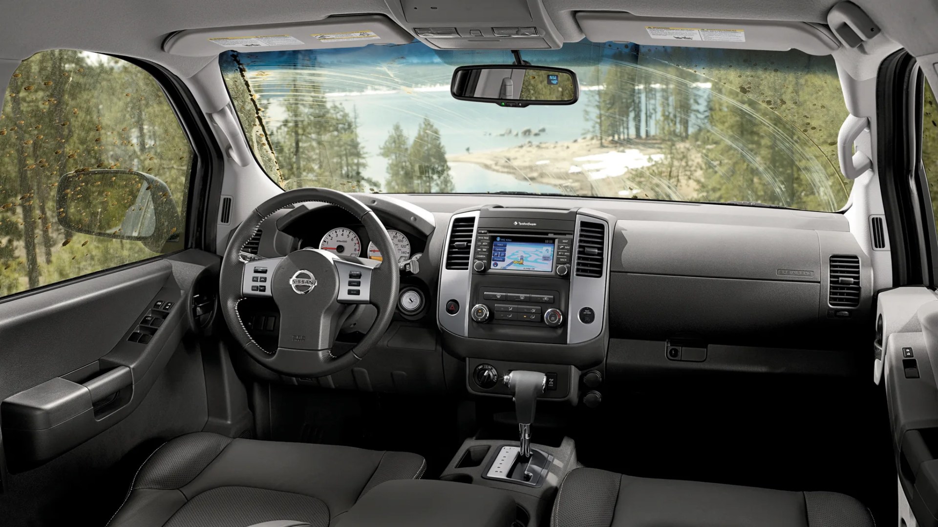 Interior view of a Nissan vehicle dashboard with black steering wheel, touchscreen display, and automatic gear shift.