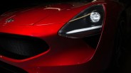 Front close-up of a red sports car showing the headlight, grille, and hood emblem.