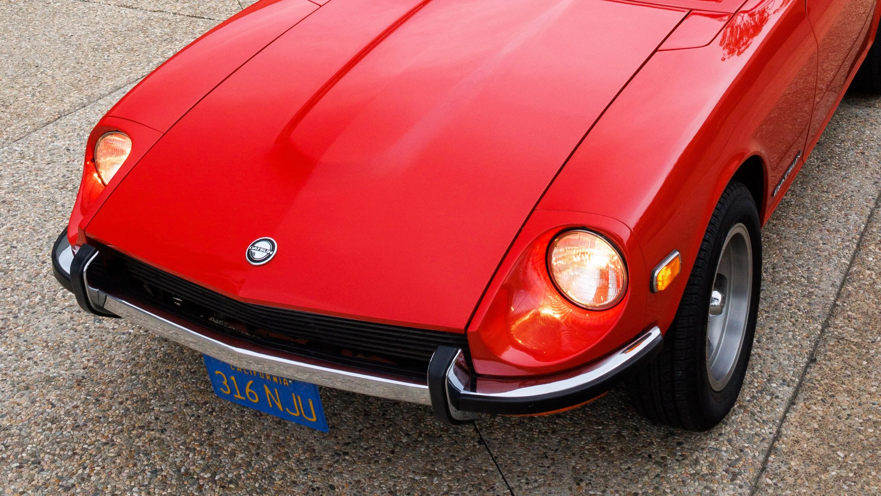 Front view of a red Datsun car with round headlights on a gravel surface.