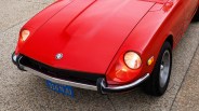 Front view of a red Datsun car with round headlights on a gravel surface.