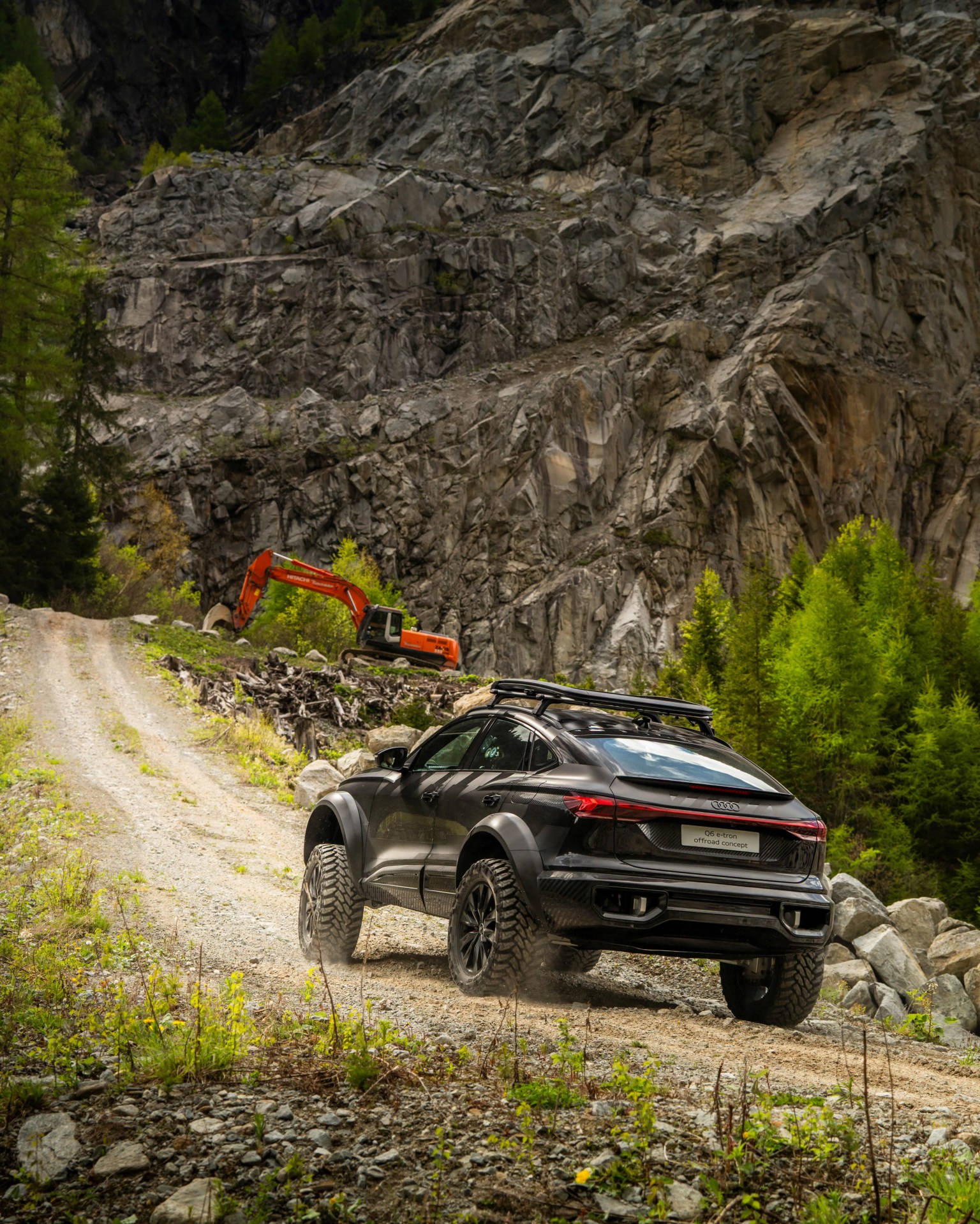 Black Audi Q6 e-tron offroad concept SUV on a gravel mountain road with rocky cliffs and green trees.